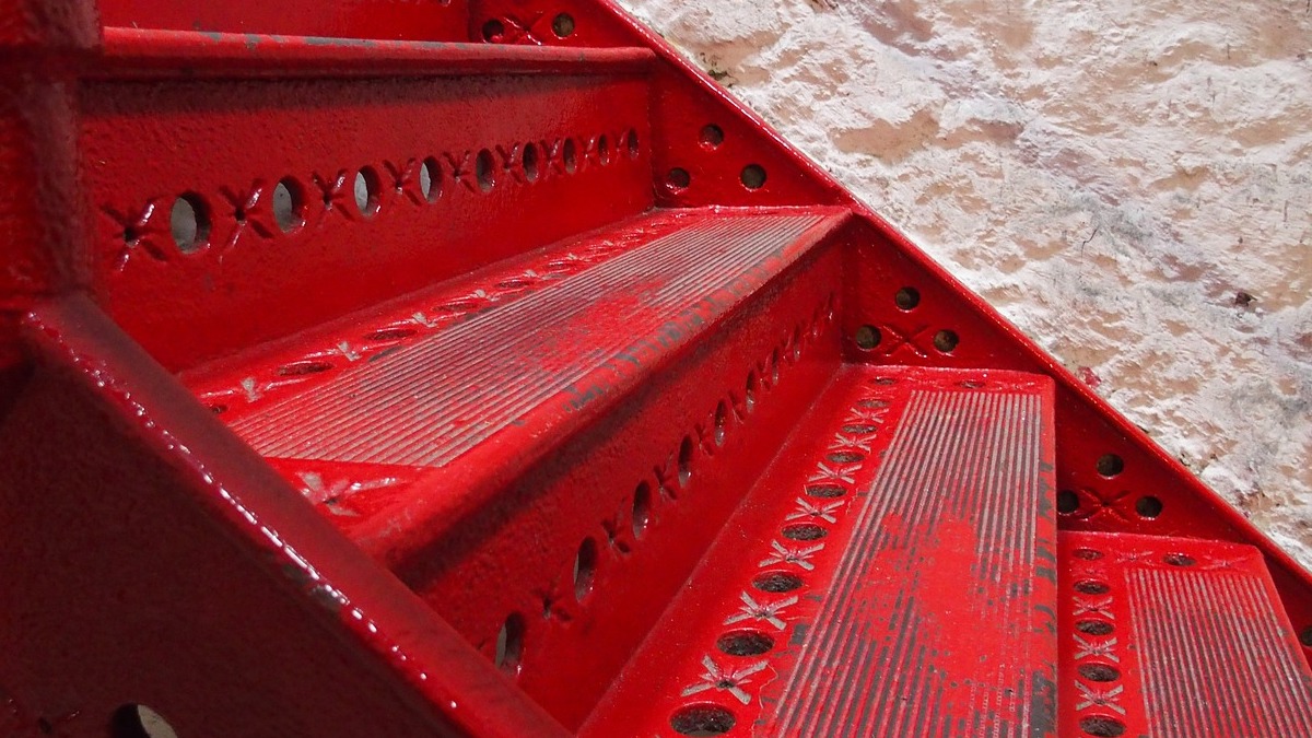 Das Bild zeigt einen Ausschnitt einer Treppe aus rotem Metall.